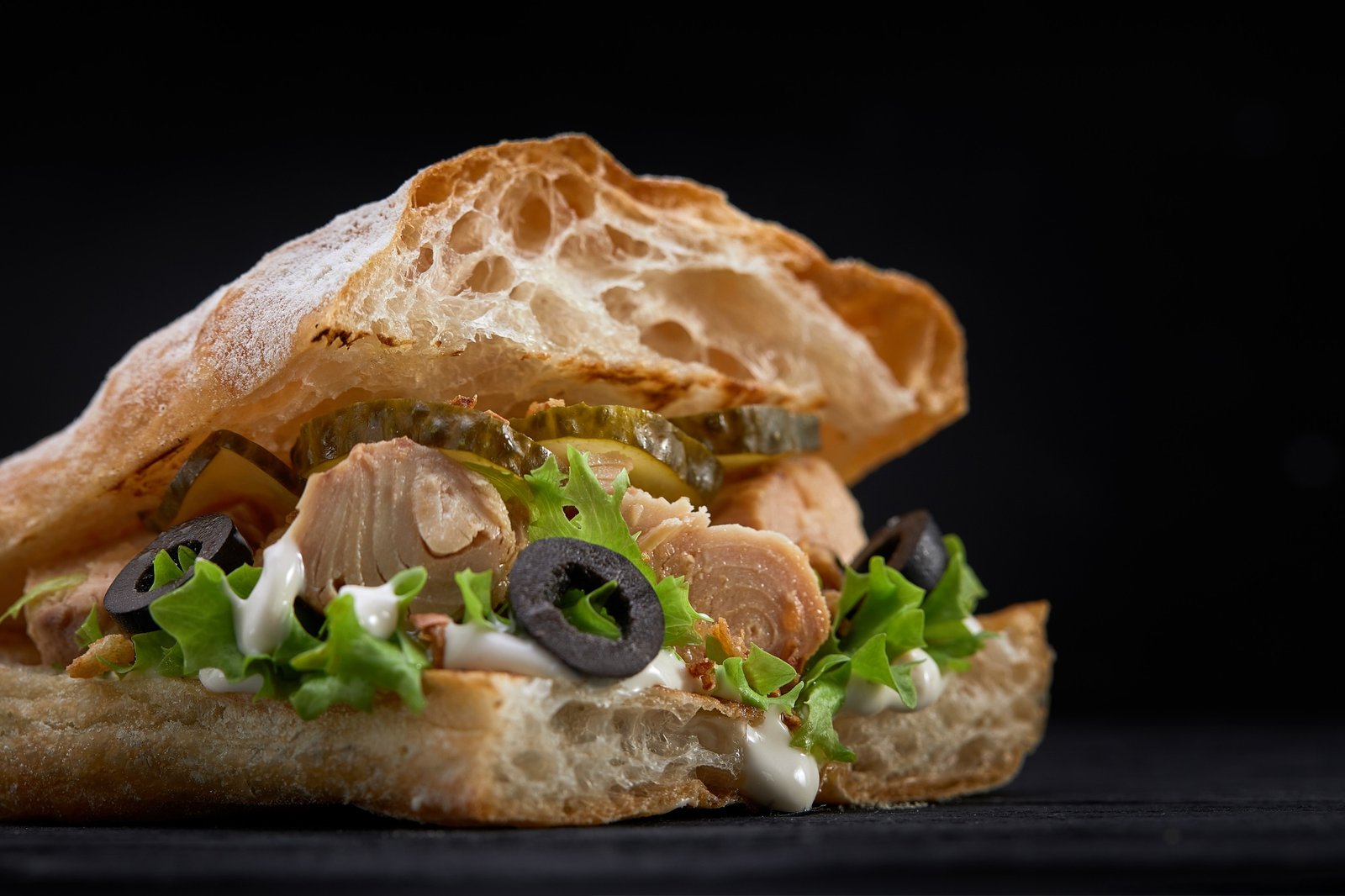 American fast food. Juicy tuna sandwich with cheese, salad and olives on a dark background. Club