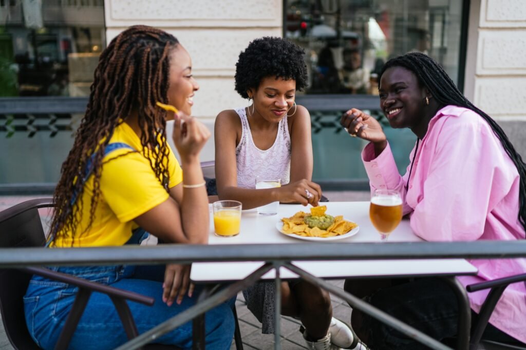 Laughing African women enjoying nachos and drinks at a city tavern terrace.