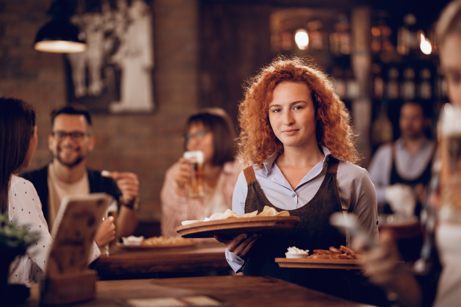 Young waitress serving food to guests in a tavern.